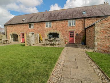 An exterior view of a brick building with a tiled roof a stone pathway grass lawn and outdoor seating at The Red Barn in Longframlington near Alnwick