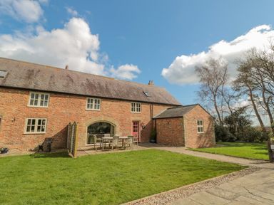 An outdoor patio area with a dining table and chairs on a grassy lawn beside a brick house at The Red Barn in Longframlington near Alnwick