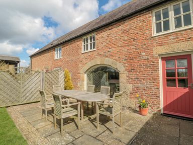 An outdoor patio area with a wooden table and six chairs beside a brick building at The Red Barn in Longframlington near Alnwick