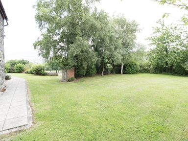 A garden with grass lawn trees and a paved walkway beside a stone building at Ddol Helyg Farmhouse in Llanrug