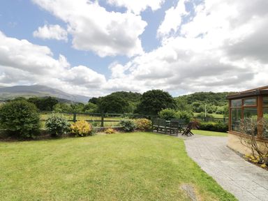 A garden with green grass shrubs and outdoor seating near a building at Ddol Helyg Farmhouse in Llanrug
