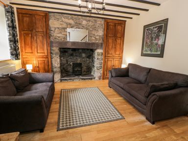 A living room with two dark sofas a stone fireplace wooden cabinets and a patterned rug at Ddol Helyg Farmhouse Llanrug