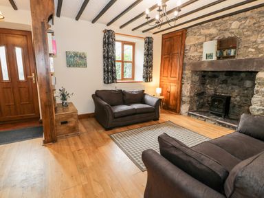A living room with two sofas a fireplace a wooden door and window at Ddol Helyg Farmhouse Llanrug