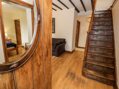 A wooden staircase next to a brown sofa and a wooden door with a round mirror at Ddol Helyg Farmhouse Llanrug