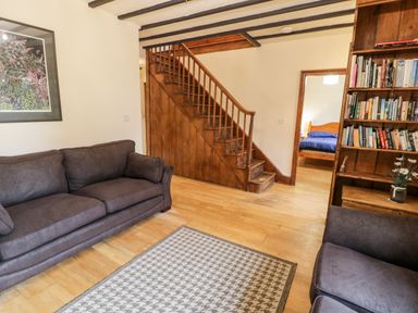 A living room with two couches a patterned rug a wooden staircase and a bookshelf at Ddol Helyg Farmhouse Llanrug