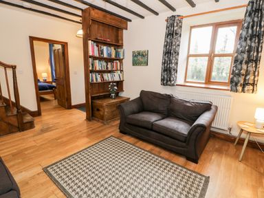 A living room with a dark sofa a patterned rug bookshelf and wooden beams at Ddol Helyg Farmhouse in Llanrug