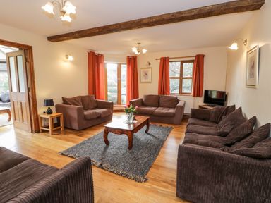 A living room with brown sofas a wooden coffee table and red curtains at Ddol Helyg Farmhouse in Llanrug