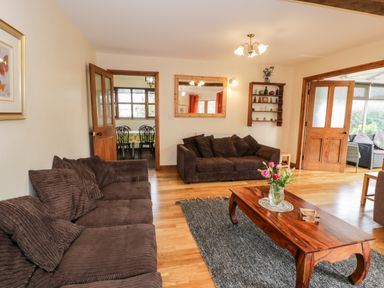 A living room with two brown sofas a wooden coffee table with flowers a gray rug and open wooden doors at Ddol Helyg Farmhouse in Llanrug