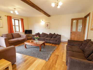 A living room with brown sofas wooden coffee table and a television at Ddol Helyg Farmhouse in Llanrug