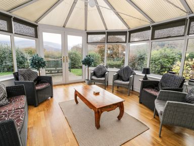 A conservatory with wicker chairs a wooden coffee table and plants outside at Ddol Helyg Farmhouse Llanrug