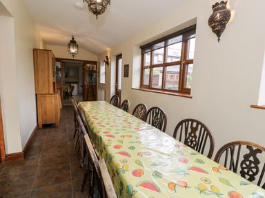 A dining room with a long table covered with a fruit-patterned tablecloth and wooden chairs at Ddol Helyg Farmhouse in Llanrug