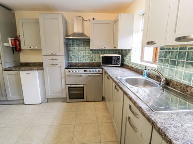 A kitchen with grey cabinets a stove microwave sink and green tiled backsplash at Ddol Helyg Farmhouse in Llanrug