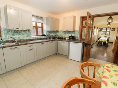A kitchen with tiled floor cabinets a countertop with appliances and a dining area visible through an open door at Ddol Helyg Farmhouse Llanrug