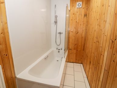 A bathroom with a bathtub shower combination and wooden wall paneling at Ddol Helyg Farmhouse in Llanrug