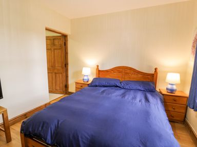 A bedroom with a wooden bed with blue bedding and two bedside tables with lamps at Ddol Helyg Farmhouse in Llanrug