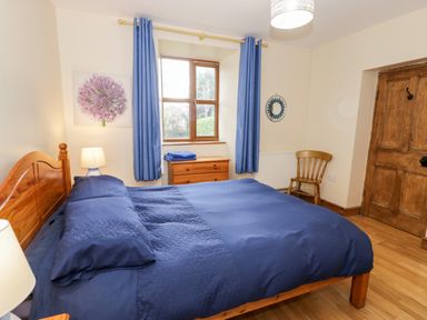 A bedroom with a blue bedspread blue curtains wooden furniture and a wooden door at Ddol Helyg Farmhouse in Llanrug