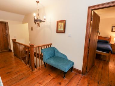 A wooden staircase landing with a blue upholstered bench a wooden door leading to a bedroom with a wooden bed and nightstand at Ddol Helyg Farmhouse in Llanrug
