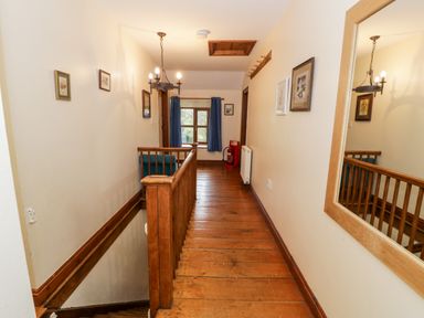 A wooden hallway with stairs and framed pictures on the walls at Ddol Helyg Farmhouse in Llanrug