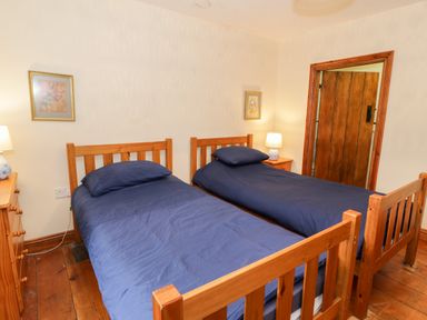 A bedroom with two wooden single beds with blue bedding and bedside tables with lamps at Ddol Helyg Farmhouse in Llanrug