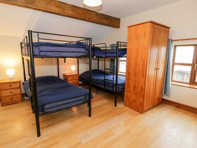 A bedroom with two bunk beds blue bedding wooden wardrobes and bedside tables with lamps at Ddol Helyg Farmhouse Llanrug