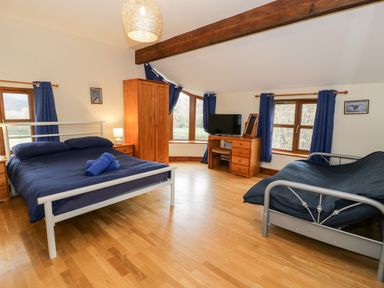 A bedroom with two beds a wooden wardrobe a desk with a television and blue curtains at Ddol Helyg Farmhouse in Llanrug