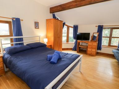 A bedroom with a blue bedspread wooden furniture and windows with blue curtains at Ddol Helyg Farmhouse Llanrug