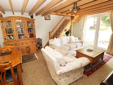 A living room with floral sofas a wooden coffee table a wooden dining table a wooden cabinet and stairs at Morfa Isaf Cottage in Llangrannog