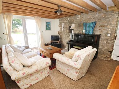 A living room with floral sofas a wooden coffee table a piano and exposed stone wall at Morfa Isaf Cottage in Llangrannog