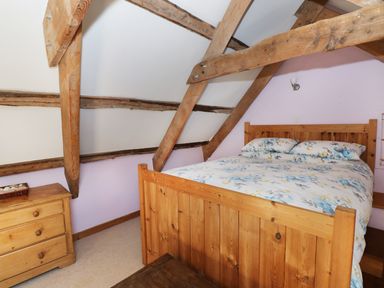 A bedroom with a wooden bed and a dresser under exposed wooden beams at Morfa Isaf Cottage in Llangrannog
