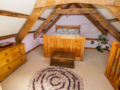 A bedroom with a wooden bed chest dresser and a plant at Morfa Isaf Cottage in Llangrannog
