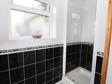 A bathroom with a shower enclosure and a window with a small basket on the sill at Morfa Isaf Cottage in Llangrannog