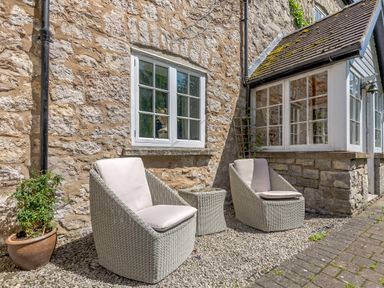 Two outdoor wicker chairs with cushions and a small table between them outside a stone wall house at Distyll Llanfwrog near Ruthin