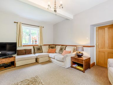 A living room with a sectional sofa cushions a wooden side table with a lamp a television and a window at Distyll in Llanfwrog near Ruthin