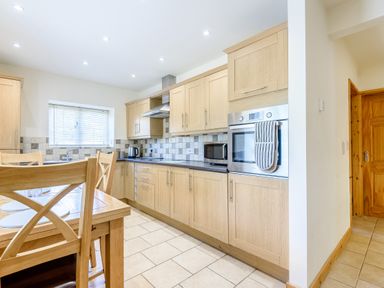 A kitchen with wooden cabinets dining table chairs and built in oven at Distyll in Llanfwrog near Ruthin