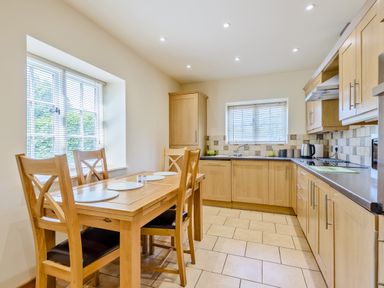 A kitchen with wooden cabinets dining table and chairs near windows at Distyll Llanfwrog near Ruthin