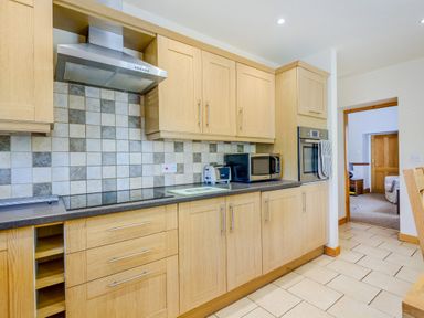 A kitchen with wooden cabinets stove oven microwave and toaster at Distyll in Llanfwrog near Ruthin