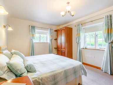 A bedroom with a bed pillows wardrobe and windows with curtains at Distyll Llanfwrog near Ruthin