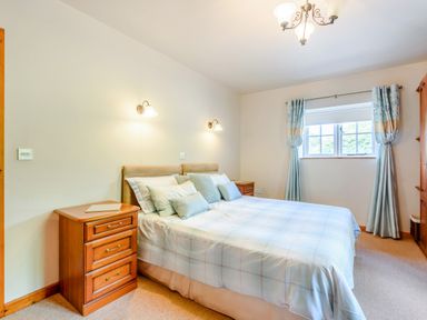 A bedroom with a double bed with pillows bedside tables with lamps and a window with curtains at Distyll in Llanfwrog near Ruthin