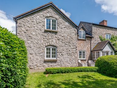 Stone house with white windows green bushes lawn and outdoor seating at Distyll Llanfwrog near Ruthin