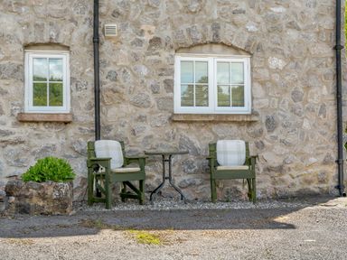Two green wooden chairs and a small table outside a stone wall building at Distyll in Llanfwrog near Ruthin