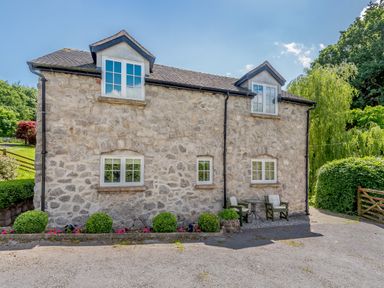 Exterior view of a stone cottage with white framed windows two chairs and a small table outside in a garden at Distyll Llanfwrog near Ruthin