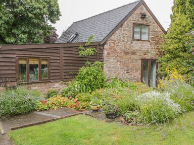A garden with various plants and flowers in front of a stone and wood cottage at Pembridge Cottage in Welsh Newton