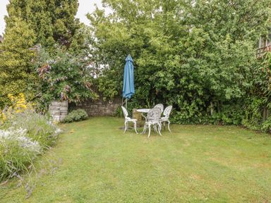 A garden with grass and white outdoor table and chairs with a blue umbrella at Pembridge Cottage in Welsh Newton