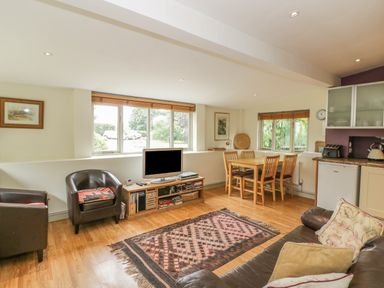 A living room with leather chairs a television wooden dining table and kitchen appliances at Pembridge Cottage in Welsh Newton
