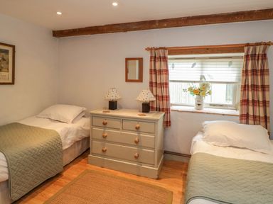 A bedroom with two single beds a chest of drawers and a window with flowers at Pembridge Cottage in Welsh Newton