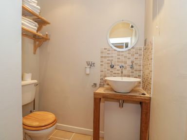 A bathroom with a toilet wooden seat towel rack and a round mirror above a sink at Pembridge Cottage in Welsh Newton