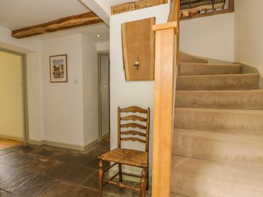 An entryway with carpeted stairs wooden chair stone floor and framed picture on wall at Pembridge Cottage in Welsh Newton