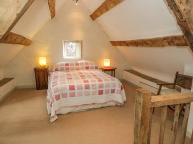 A bedroom with a bed covered by a patterned quilt two bedside tables with lamps and exposed wooden beams at Pembridge Cottage in Welsh Newton