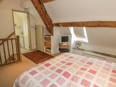 A bedroom with a bed covered in a patchwork quilt near a small TV and fan under a slanted ceiling at Pembridge Cottage in Welsh Newton