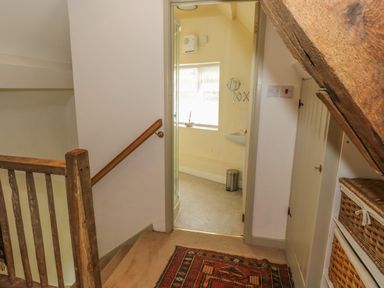A hallway with a wooden railing leading to a bathroom with a shower and a window at Pembridge Cottage in Welsh Newton